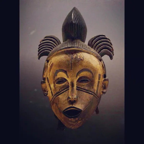Anthropomorphic mask Igbo or Idoma culture, Nigeria 20th century Wood, textile, pigments. Light colored female face with sculptural details, eyebrows, eyes, ears, scars are outlined in black. The open mouth reveals a row of tightly packed teeth. Scarifi