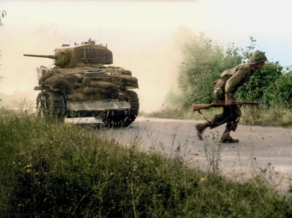 A Stuart light tank, fitted with a hedge cute and heavily sandbagged against ‘panzerfausts’, supports US infantry in the bocage, July, 1944.